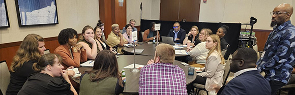 Attendees from Michigan gather around two round tables during the state work session.